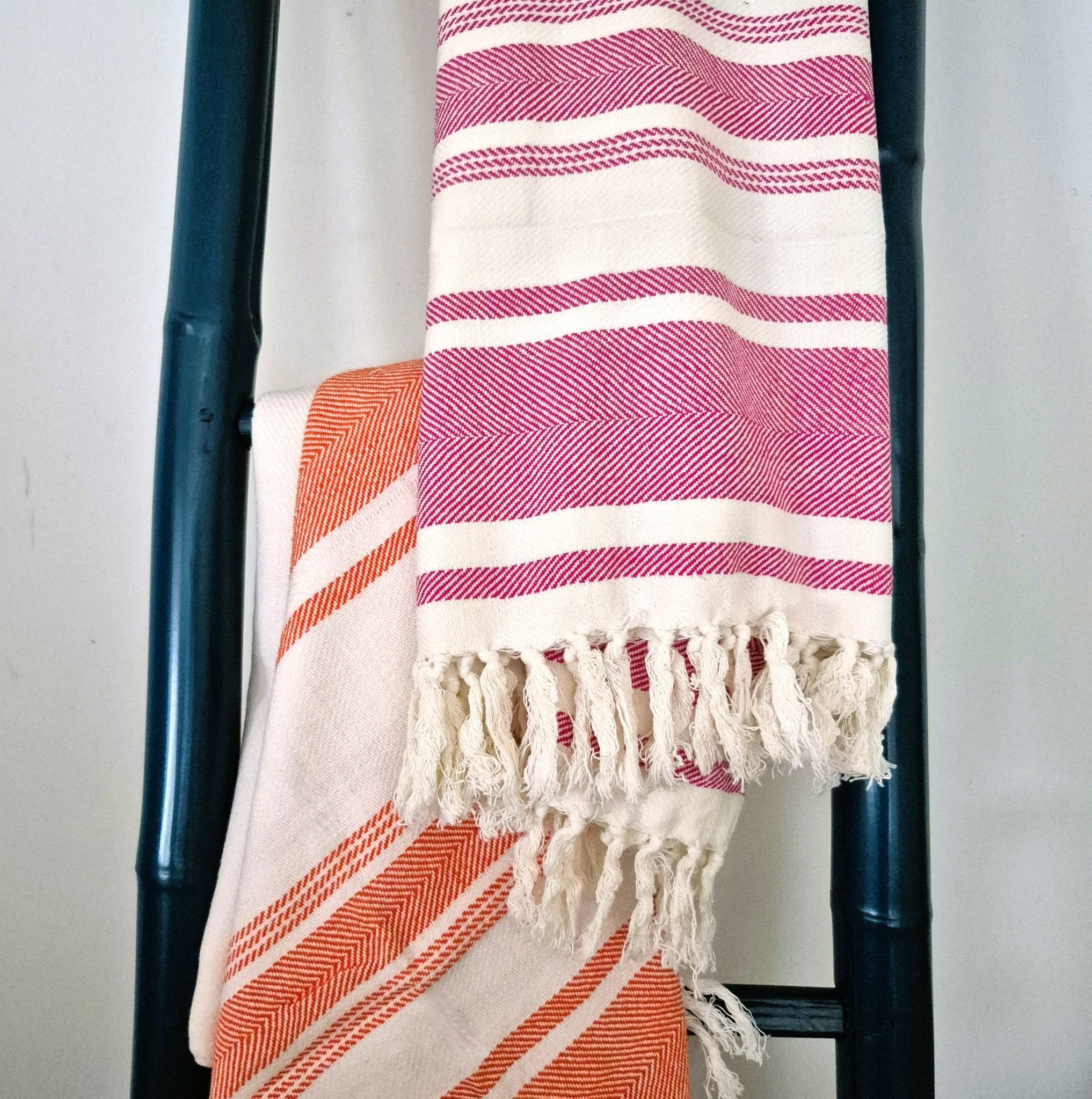 Striped towels in pink and orange draped over a towel ladder against a white background.