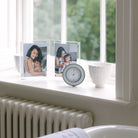 Round light blue and silver alarm clock, grey velvet backing, side view